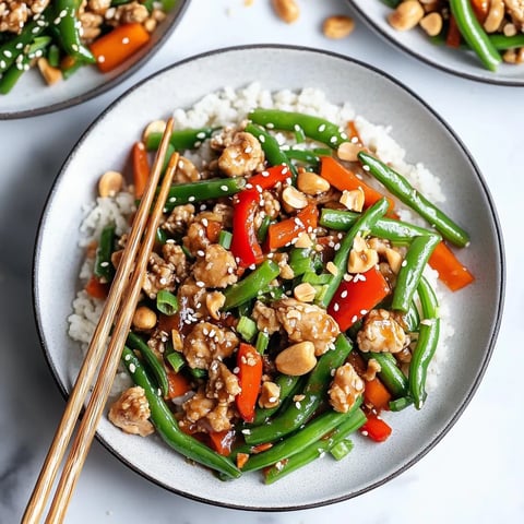 A bright plate full of chicken, green beans, and colorful veggies served next to chopsticks.
